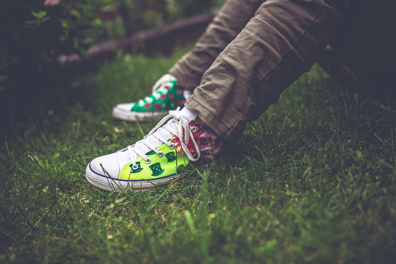 Shows a persons legs sitting on the grass with colourful chucks/shoes on